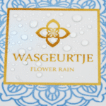 Close-up van het etiket van Wasgeurtje Flower Rain wasparfum met dauwdruppels op het goudblauwe patroon.