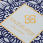 Close-up van het gouden logo op het etiket van Wasgeurtje Full Moon wasparfum, met blauwe patroonrand en fijne glansdetails.