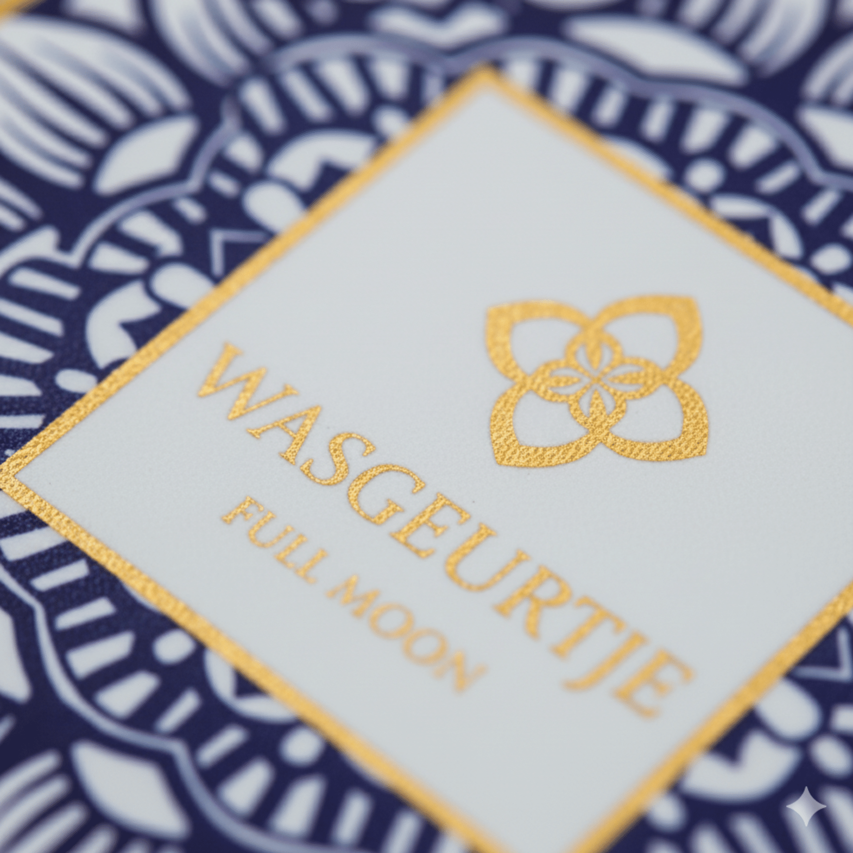 Close-up van het gouden logo op het etiket van Wasgeurtje Full Moon wasparfum, met blauwe patroonrand en fijne glansdetails.