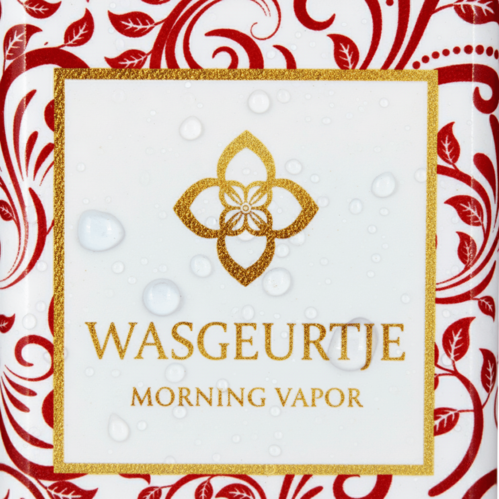 Close-up van het etiket van Wasgeurtje Morning Vapor wasparfum met gouden logo, sierlijke rode krullen en dauwdruppels op het oppervlak.