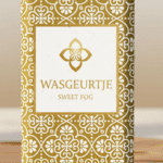 Close-up van het gouden patroon en logo van Wasgeurtje Sweet Fog wasparfum met subtiele waterdruppels — toont de hoogwaardige afwerking en premium uitstraling van het merk.