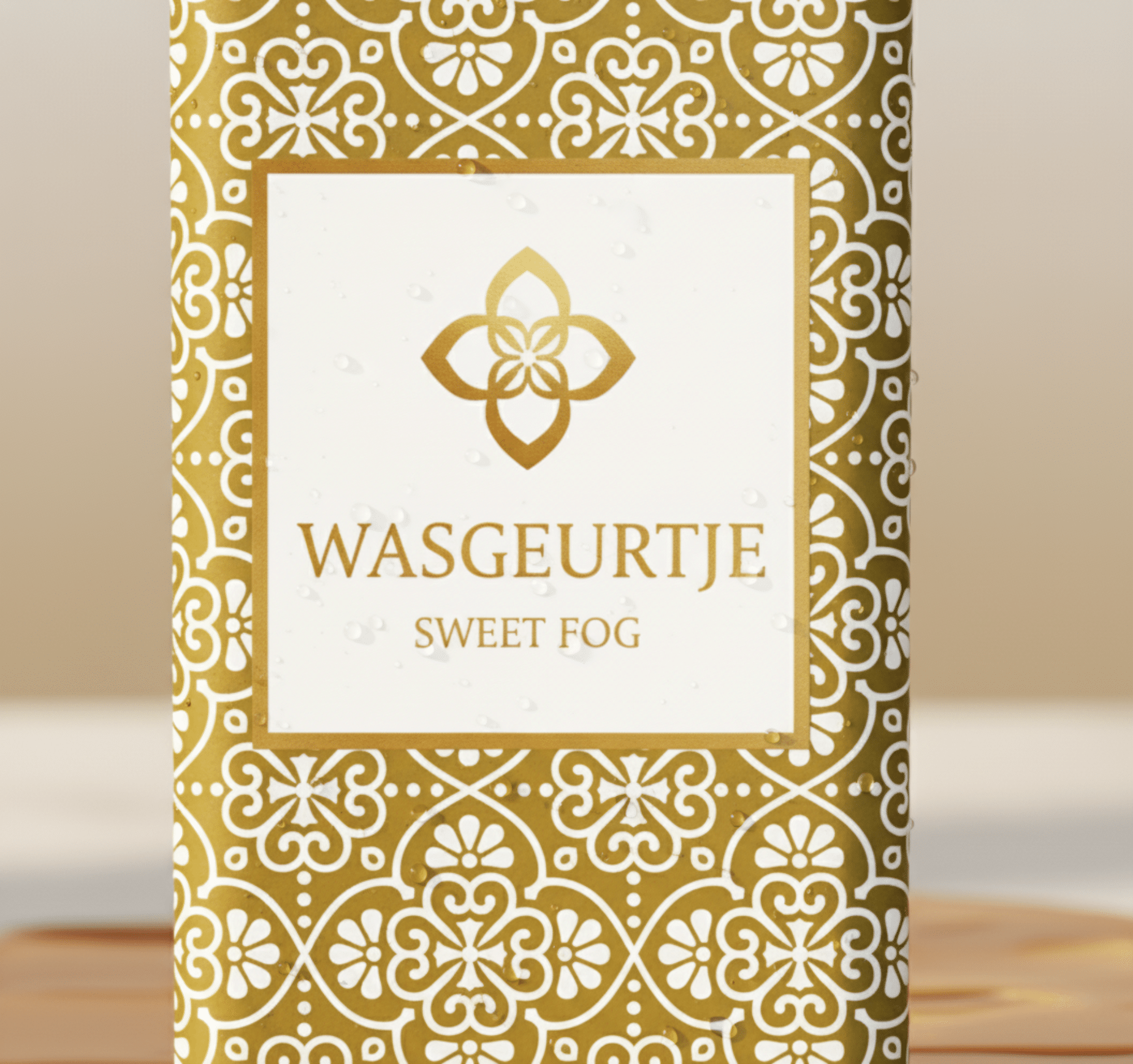 Close-up van het gouden patroon en logo van Wasgeurtje Sweet Fog wasparfum met subtiele waterdruppels — toont de hoogwaardige afwerking en premium uitstraling van het merk.