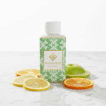 Flesje Wasgeurtje Ylang Scent wasparfum op marmeren oppervlak met sappige schijfjes citroen, sinaasappel en groene appel — een frisse en levendige presentatie die de fruitige topnoten van deze luxe wasparfum benadrukt.