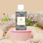 Wasgeurtje White Musk wasmiddel op een roze podium met zwarte en witte patronen, omgeven door roze bloemen en rotsen.